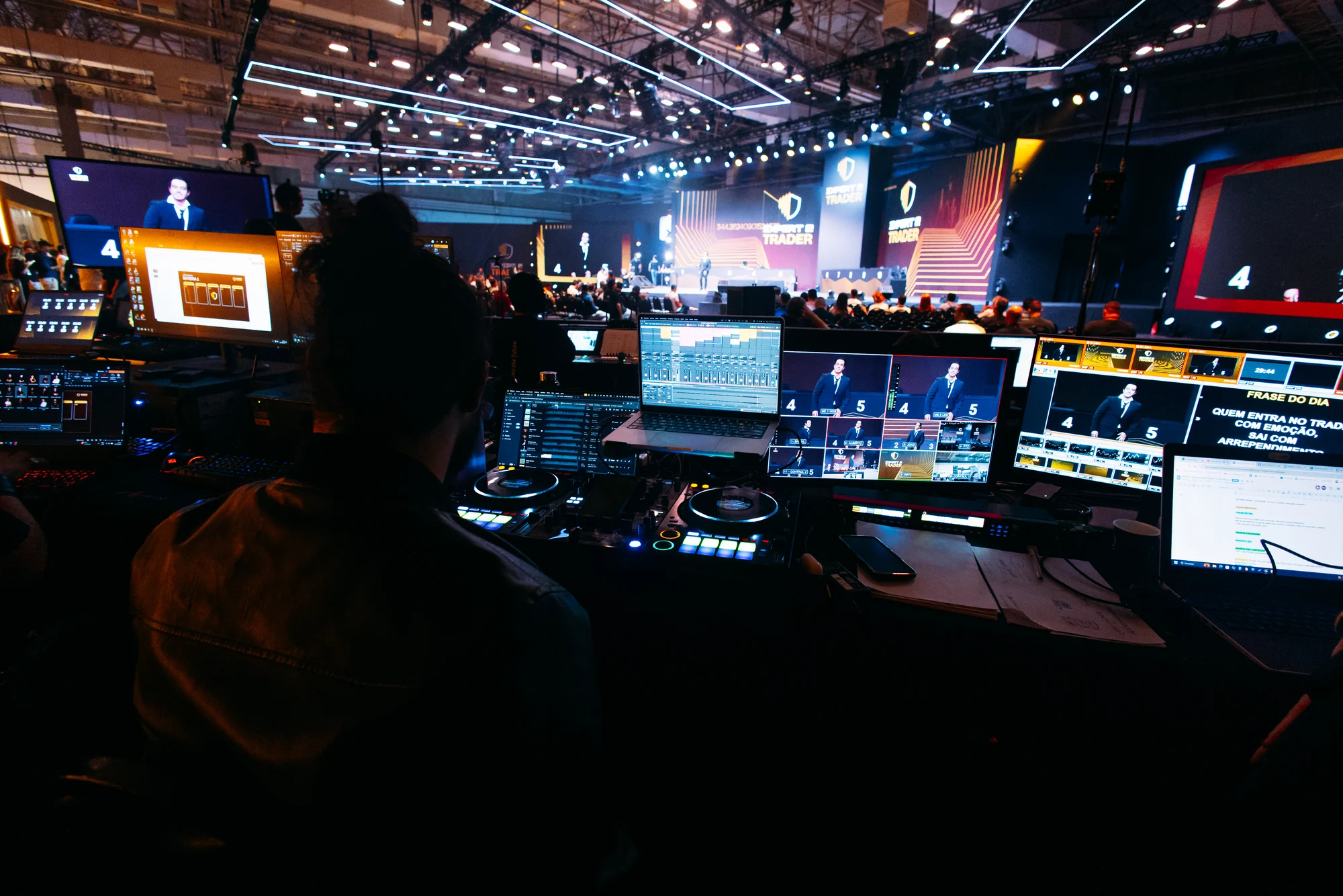Bastidores técnicos com monitores de controle e vista para o palco do evento